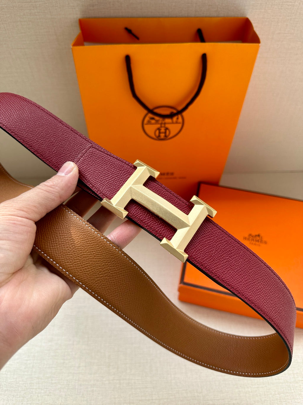 Hermes belt showing burgundy strap, gold-tone buckle, and tan inner lining