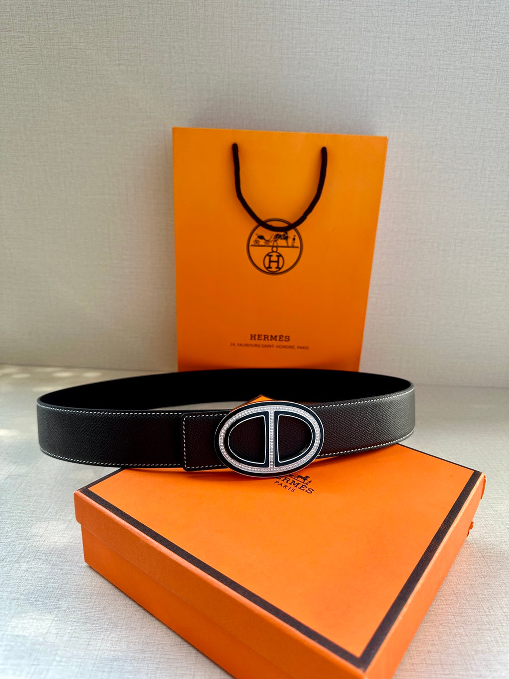 Hermes belt with dark leather strap and double H buckle on a centered display