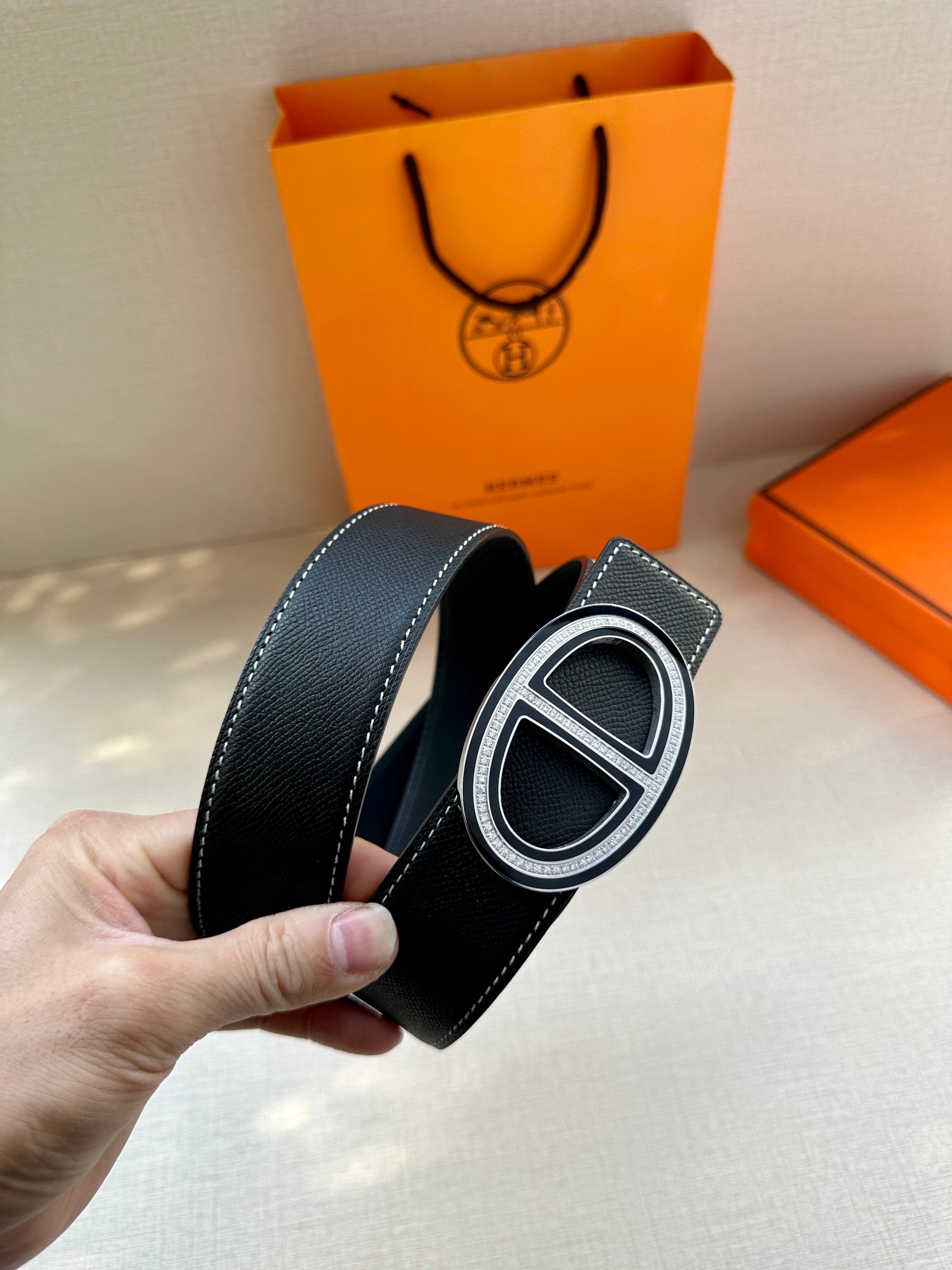Dark leather belt with oval H buckle, side angle showing strap edge