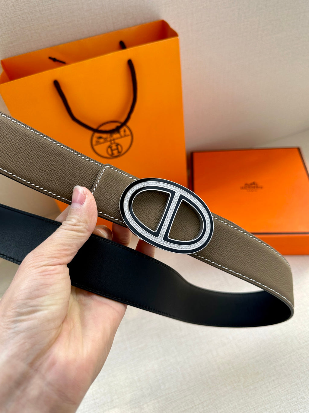 Taupe leather belt with silver-tone oval buckle, black lining showing