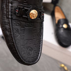 Black leather loafer upper close-up with gold Medusa buckle and embossed motif