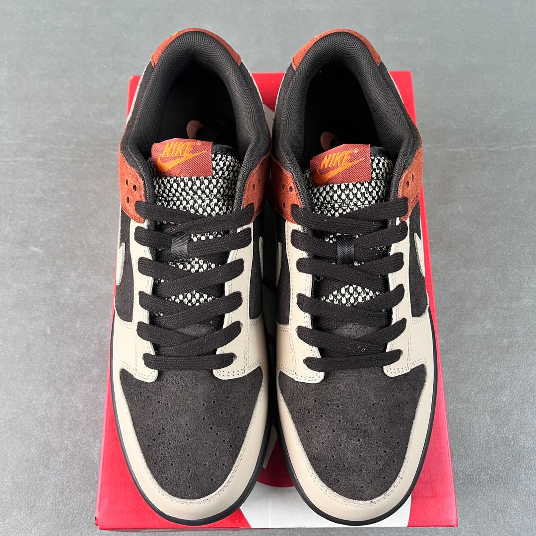 Front view of black and white low-top sneakers with orange collar accents and black laces
