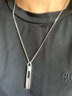 Gucci necklace pendant with silver-tone bar and logo on a chain over a dark shirt