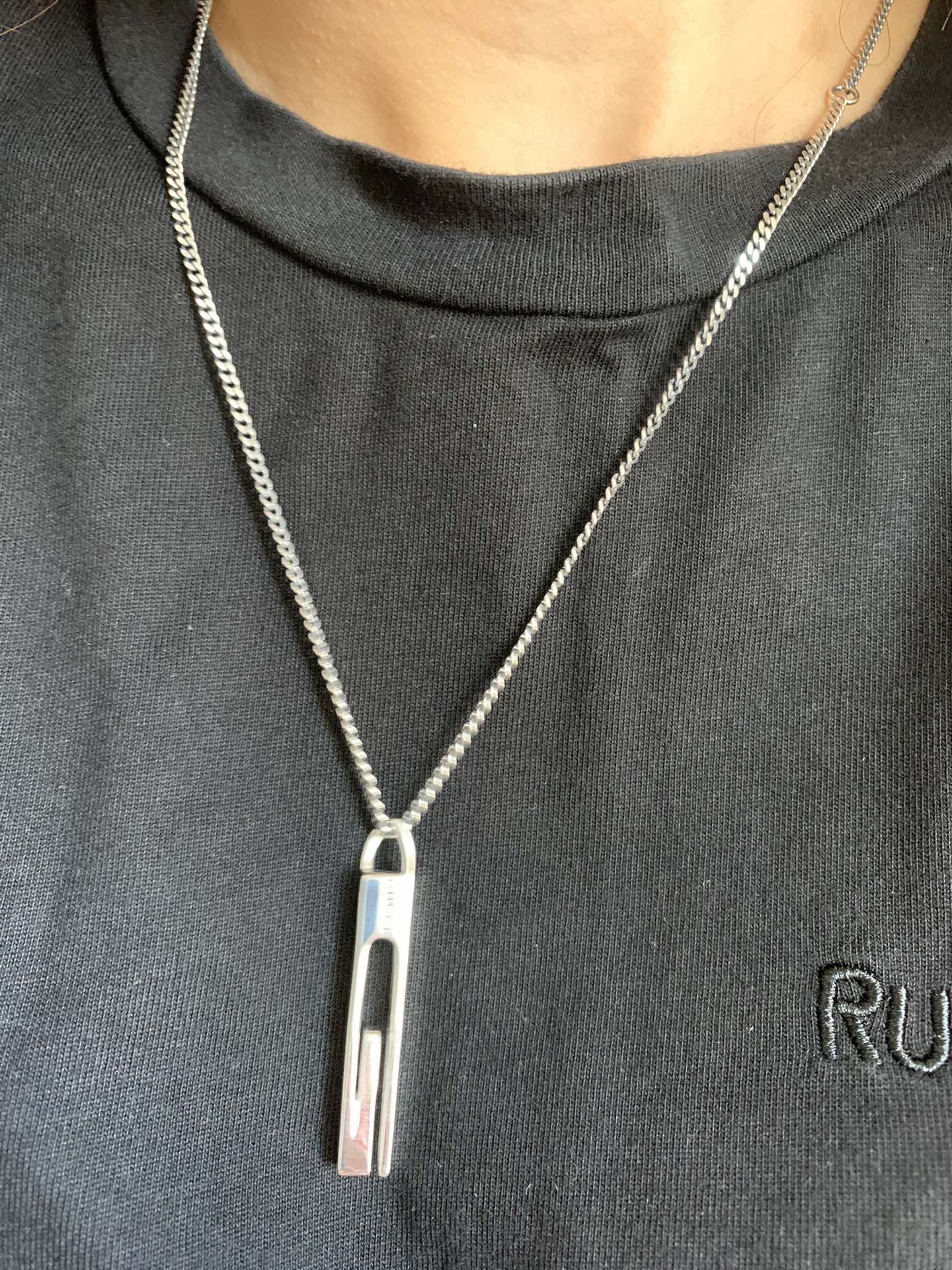 Gucci necklace pendant with silver-tone bar and logo on a chain over a dark shirt