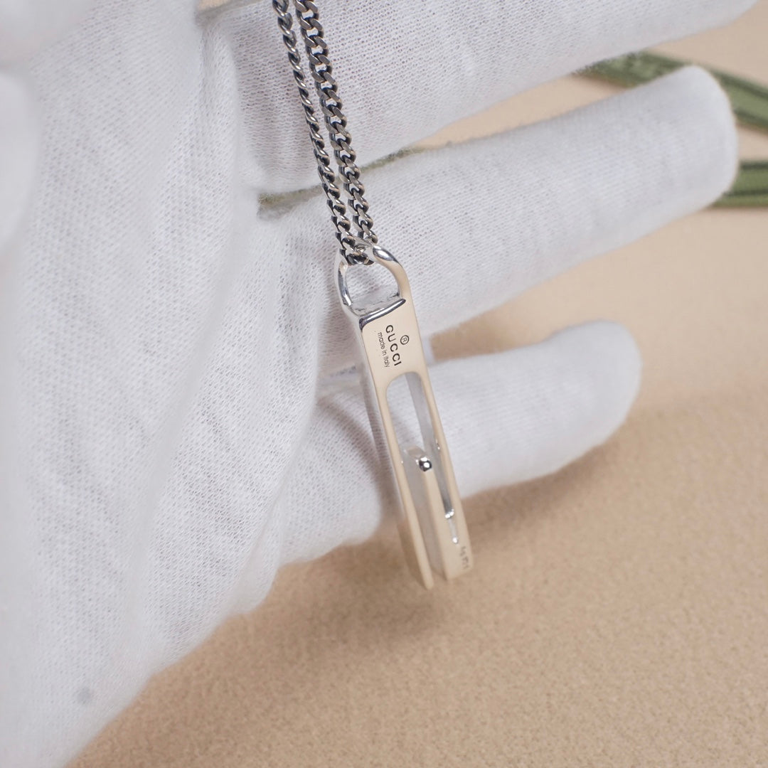 Gucci necklace pendant held in a hand, silver-tone bar with logo
