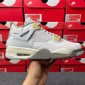 Light gray Air Jordan 4 sneaker with quilted panel and cream sole, yellow heel accents