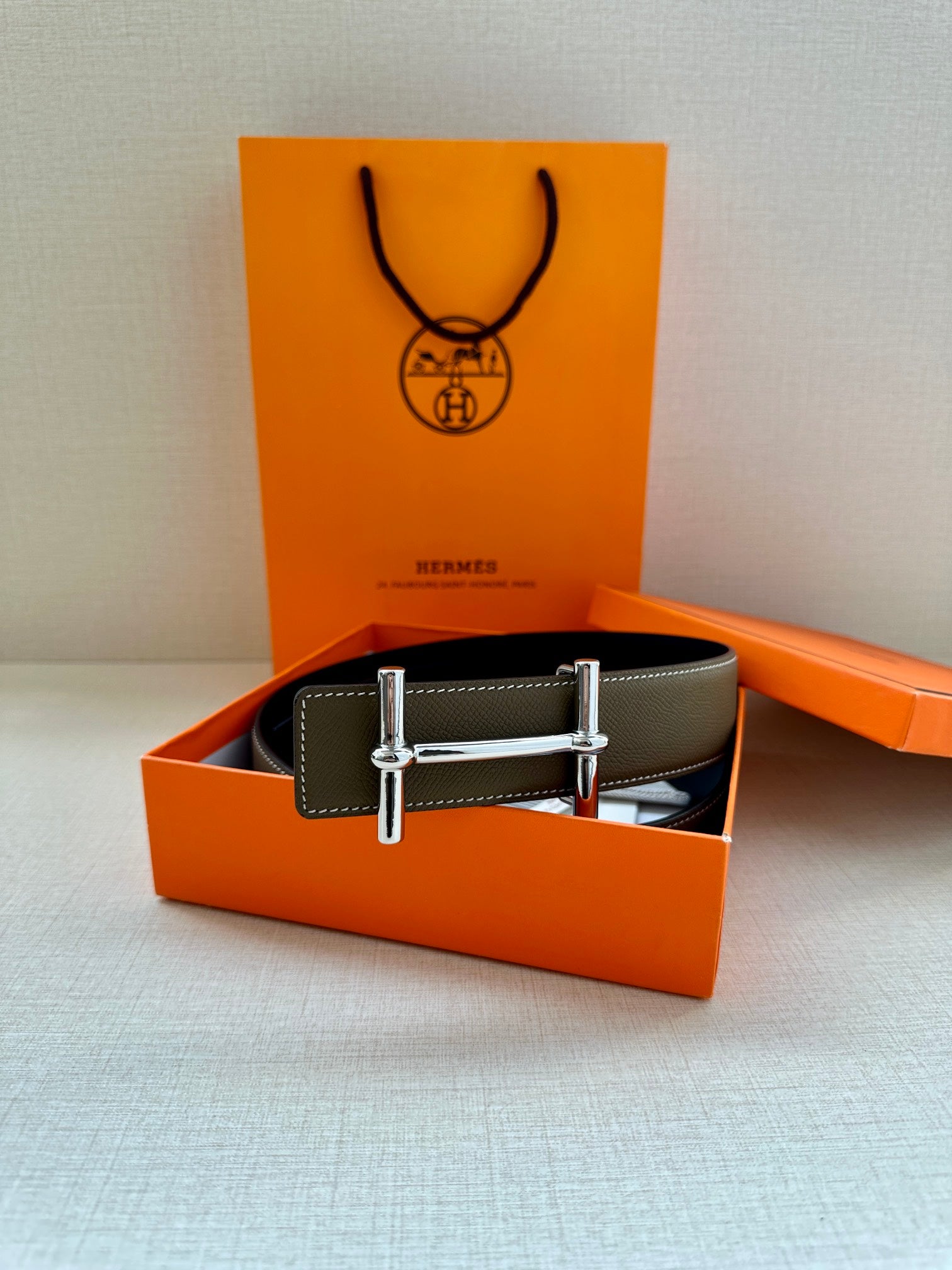 Taupe leather belt displayed in box with silver double-prong buckle