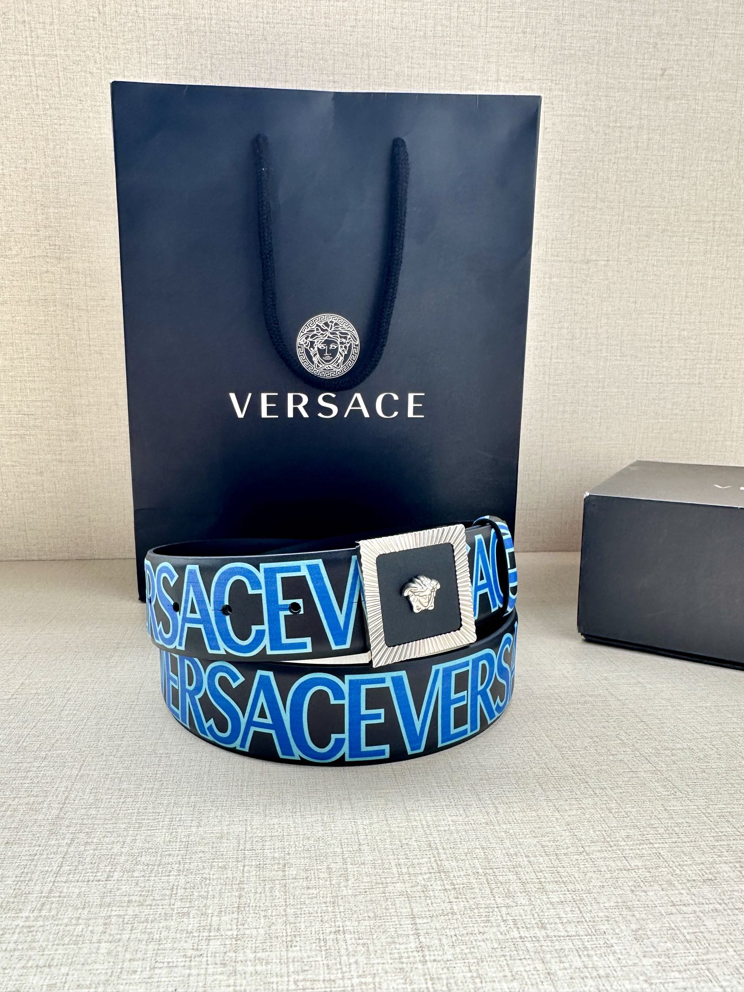 Versace logo belt featuring blue strap text and gold buckle with Medusa emblem.