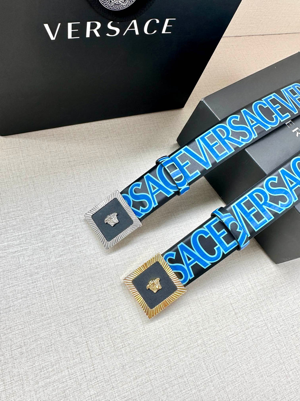 Versace logo belt pair view, blue lettering strap with gold buckle and Medusa.