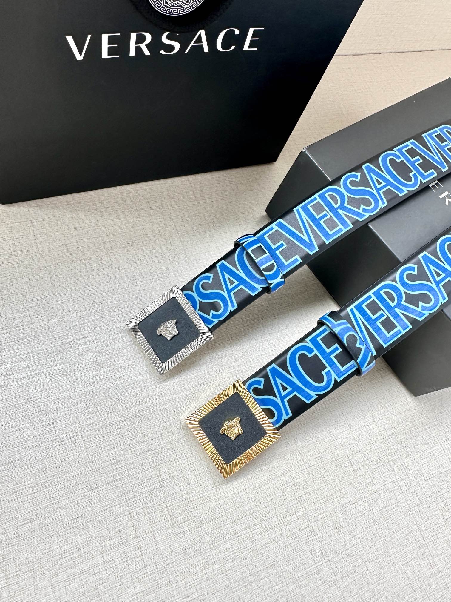Versace logo belt pair view, blue lettering strap with gold buckle and Medusa.