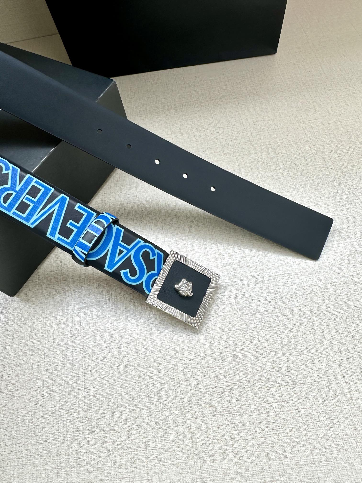 Versace belt flat lay with dark blue strap and gold buckle plate, Medusa.