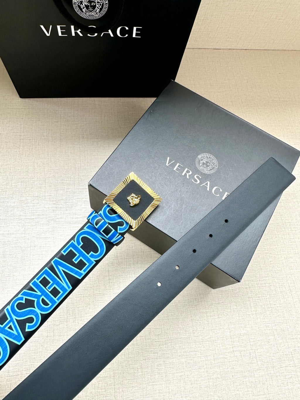 Versace belt with dark blue strap, gold buckle plaque, small white holes.