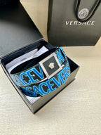 Versace logo belt inside box, blue strap with repeating lettering and gold buckle.