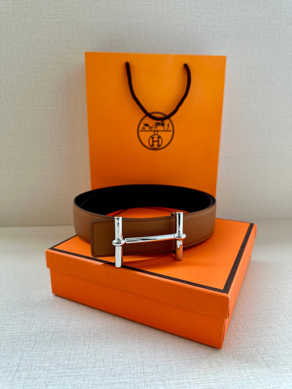 Hermes leather belt in tan with silver buckle, front view on display setup