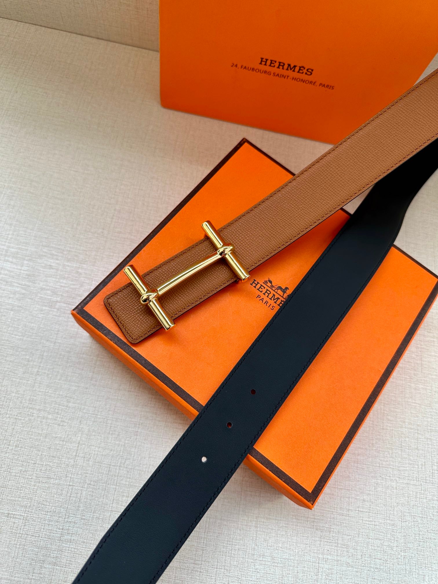 Hermes leather belt in tan with silver buckle and navy underside, flat on surface