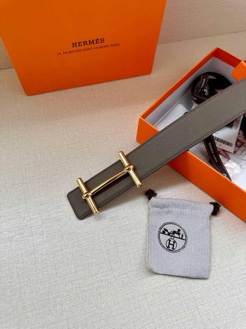 Gray leather belt with gold-toned double-bar buckle, shown near tag