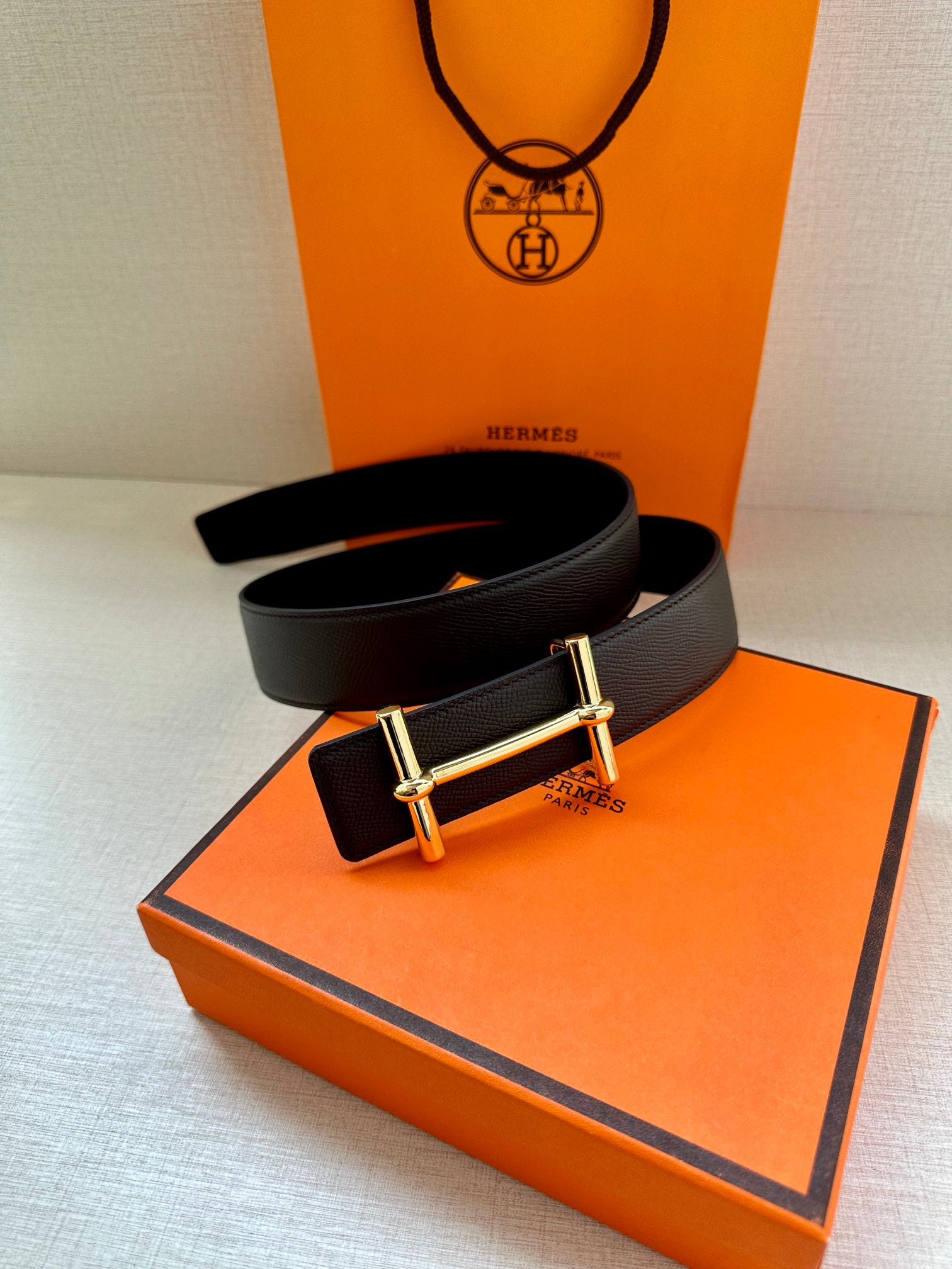 Hermes belt with dark leather strap and gold-tone double-bar buckle on box