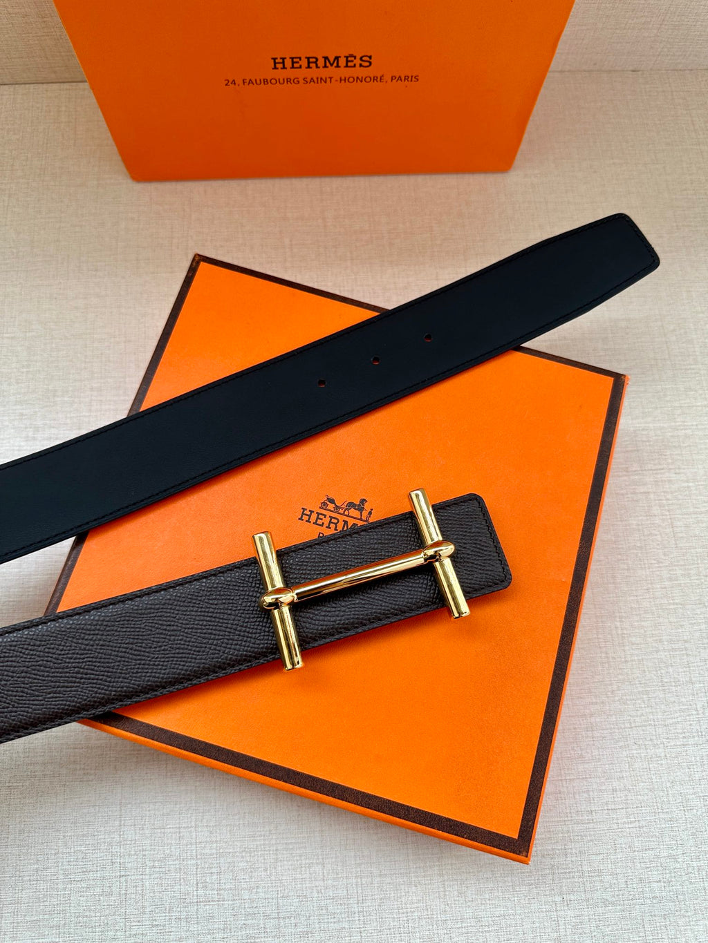 Hermes belt on black-and-orange packaging, dark leather strap with gold-tone buckle