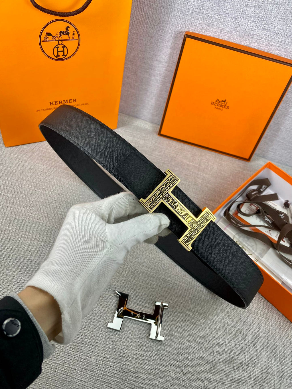 Dark leather belt with gold-tone square patterned buckle held in white glove