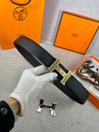 Dark leather belt with gold-tone square patterned buckle held in white glove