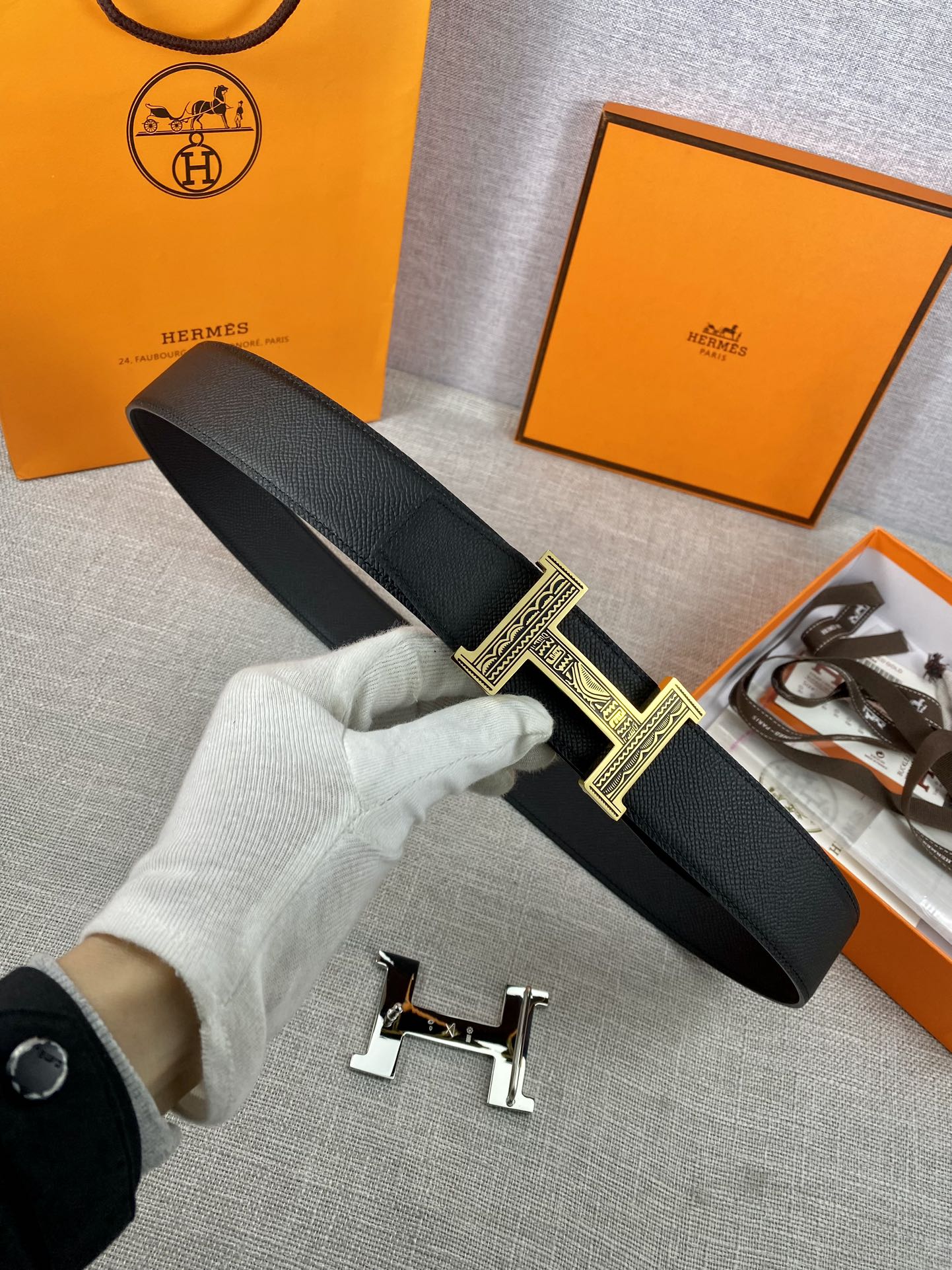 Dark leather belt with gold-tone square patterned buckle held in white glove