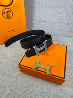 Dark leather belt with silver-tone square buckle, laid on orange accessory box