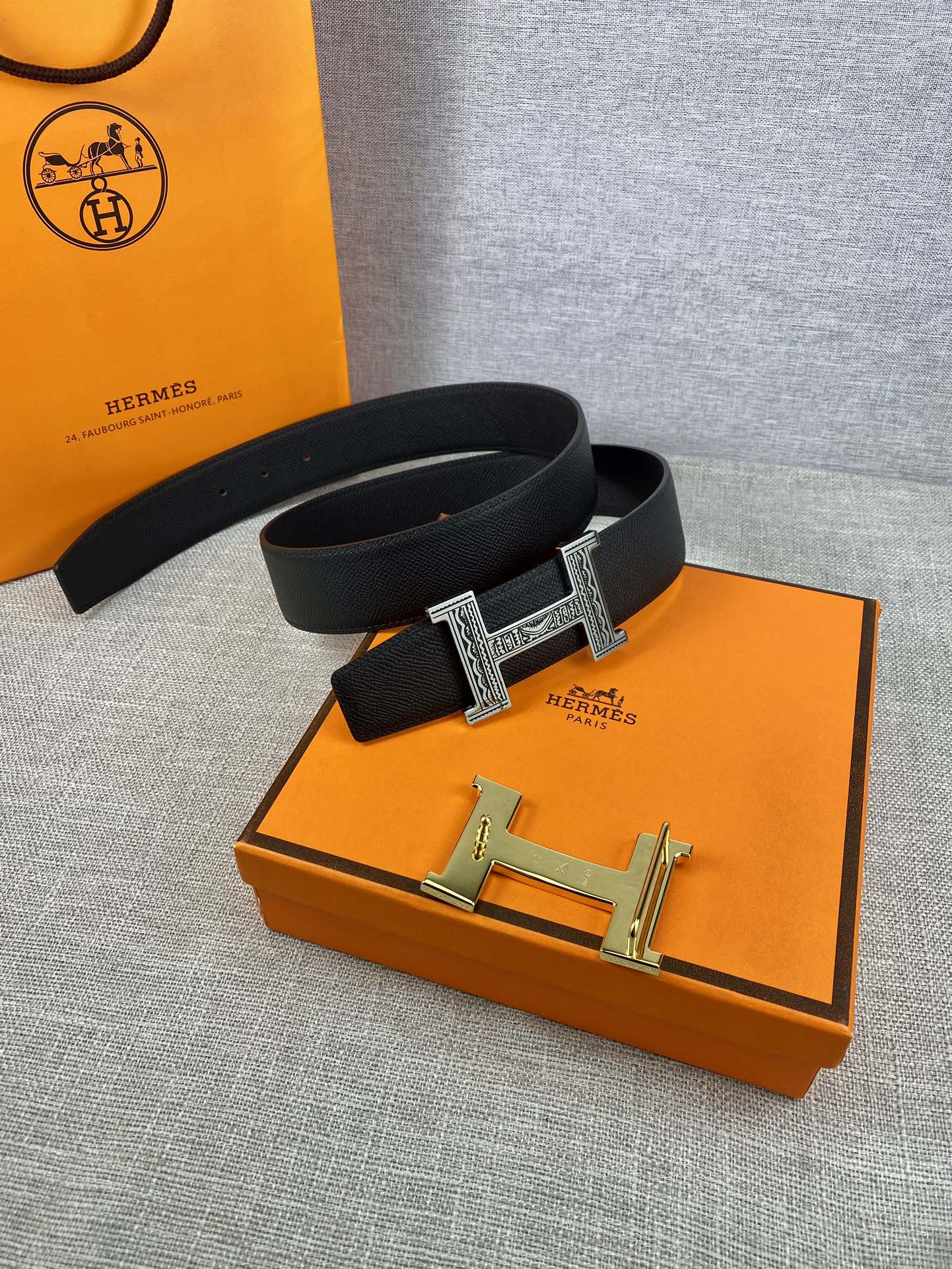 Dark leather belt with silver-tone square buckle, laid on orange accessory box