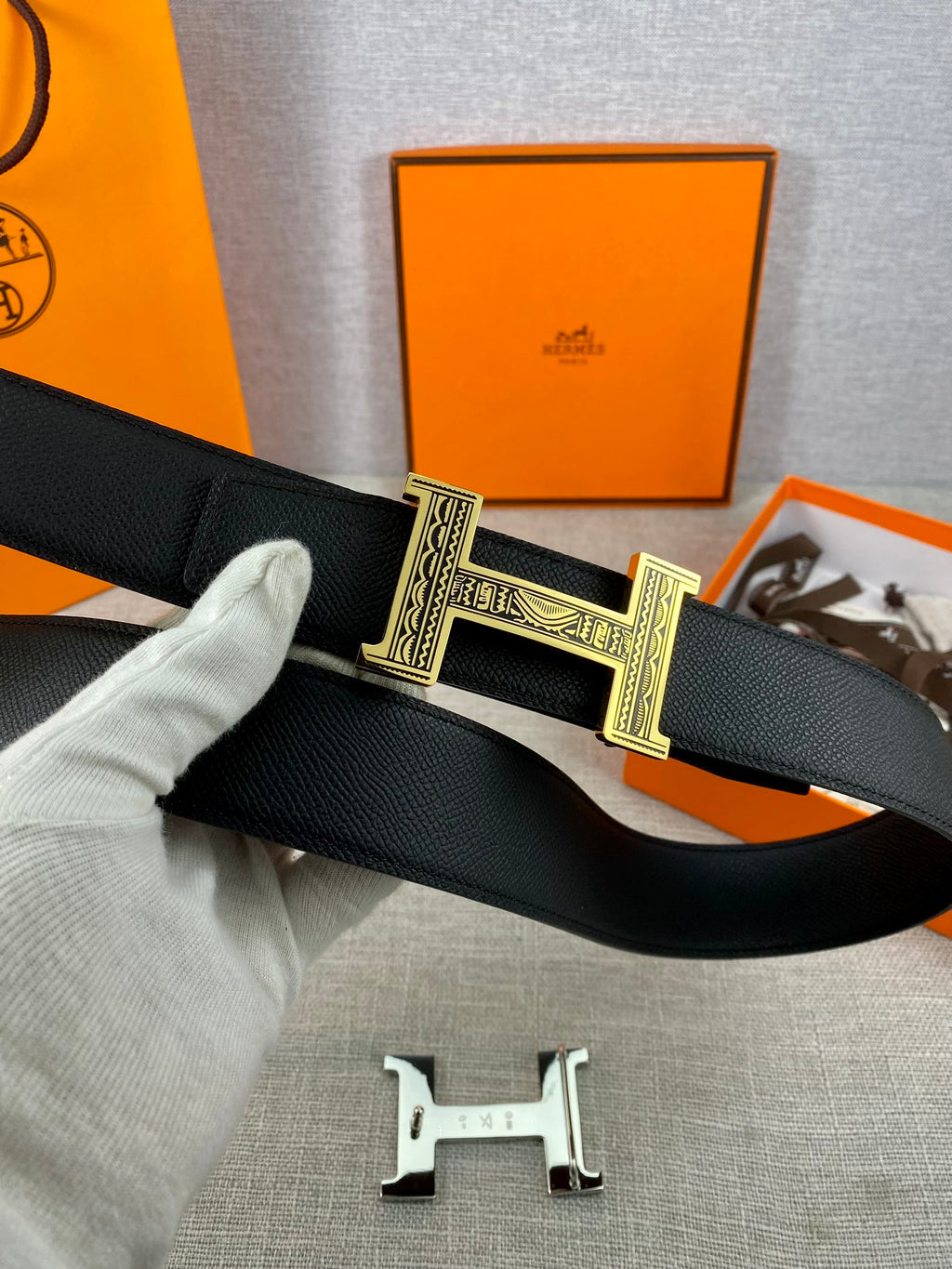 Dark leather belt with gold-tone square buckle detail, flat on light fabric