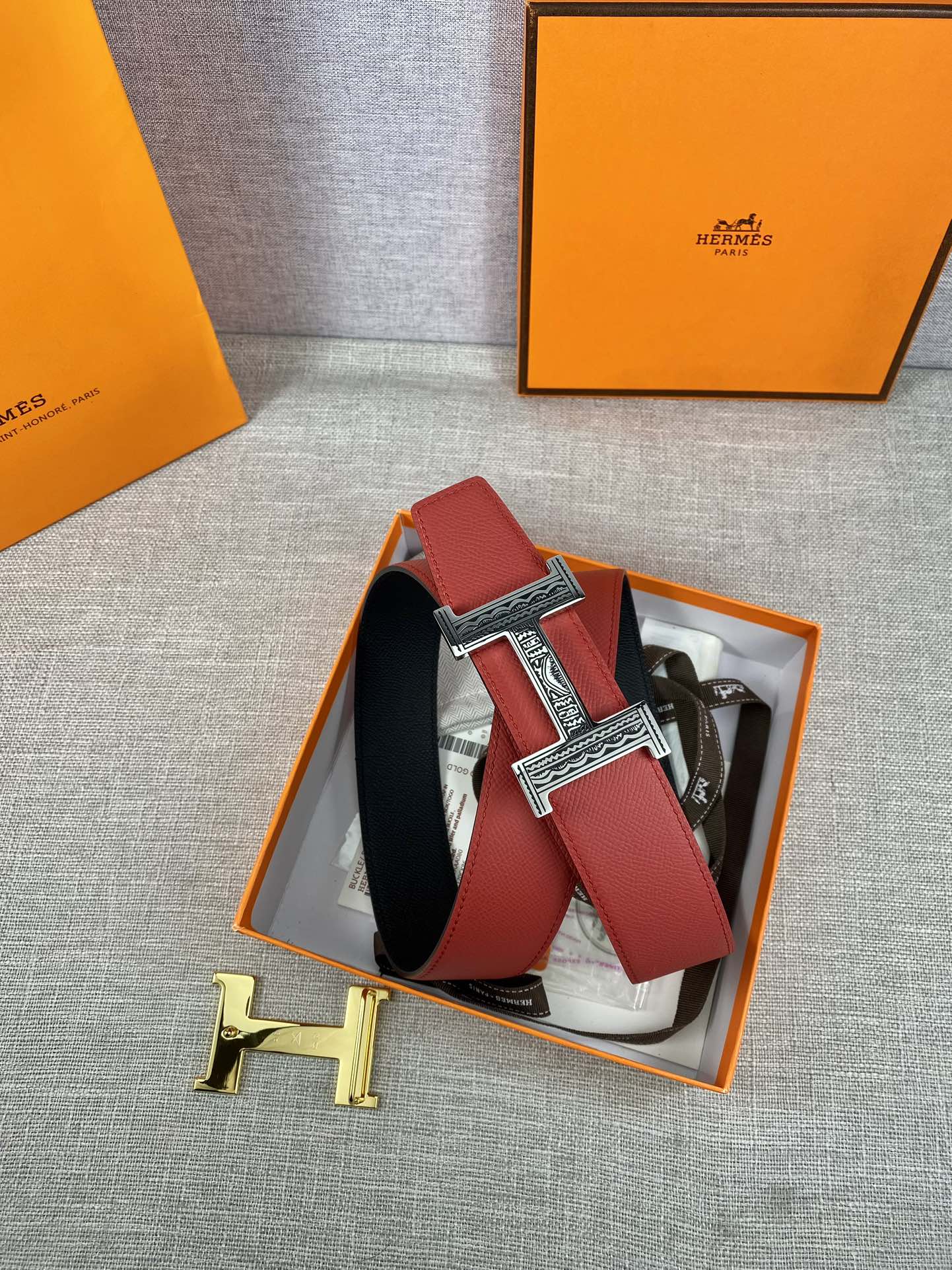 Red belt with silver engraved H buckle and black underside, displayed in orange box