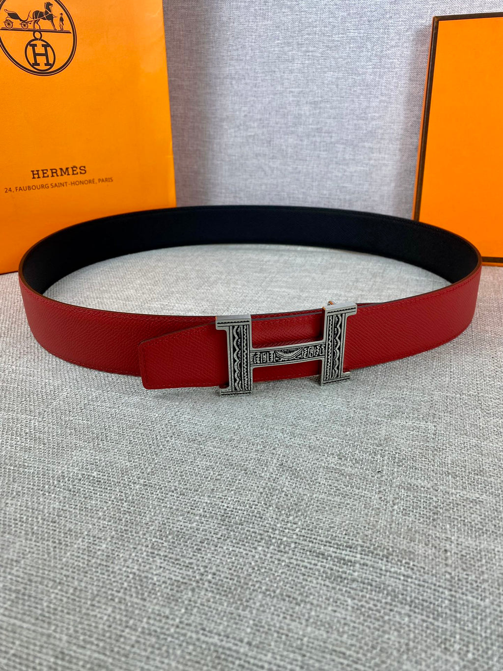 Red and black Hermes belt with silver H buckle clasp, laid on light fabric