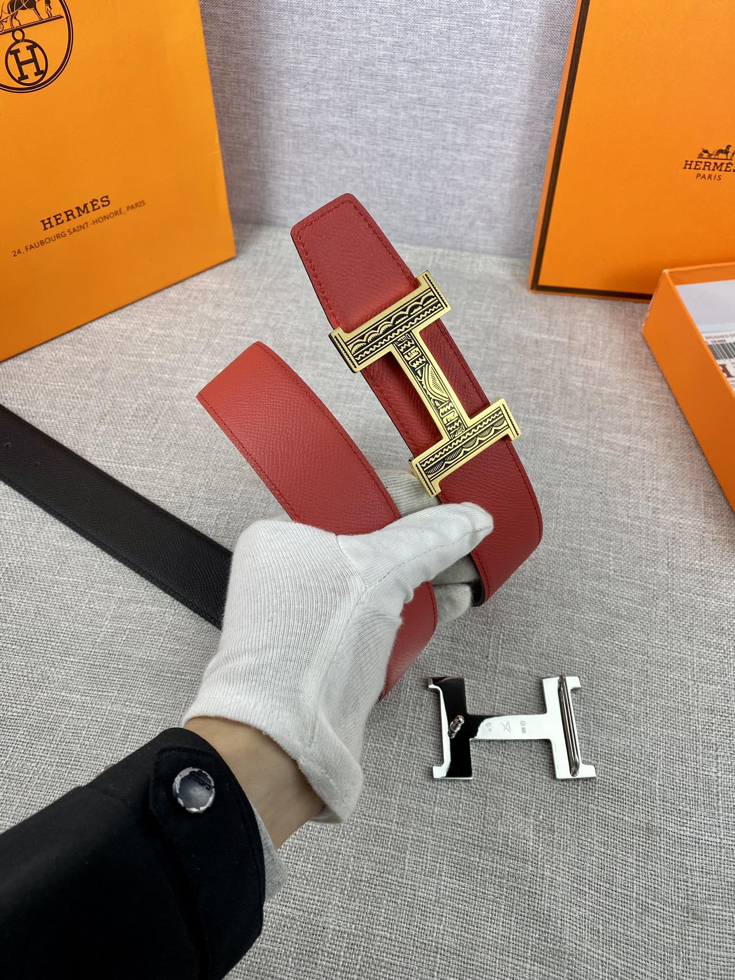 Red and black belt with silver H buckle and leather strap, held in hand