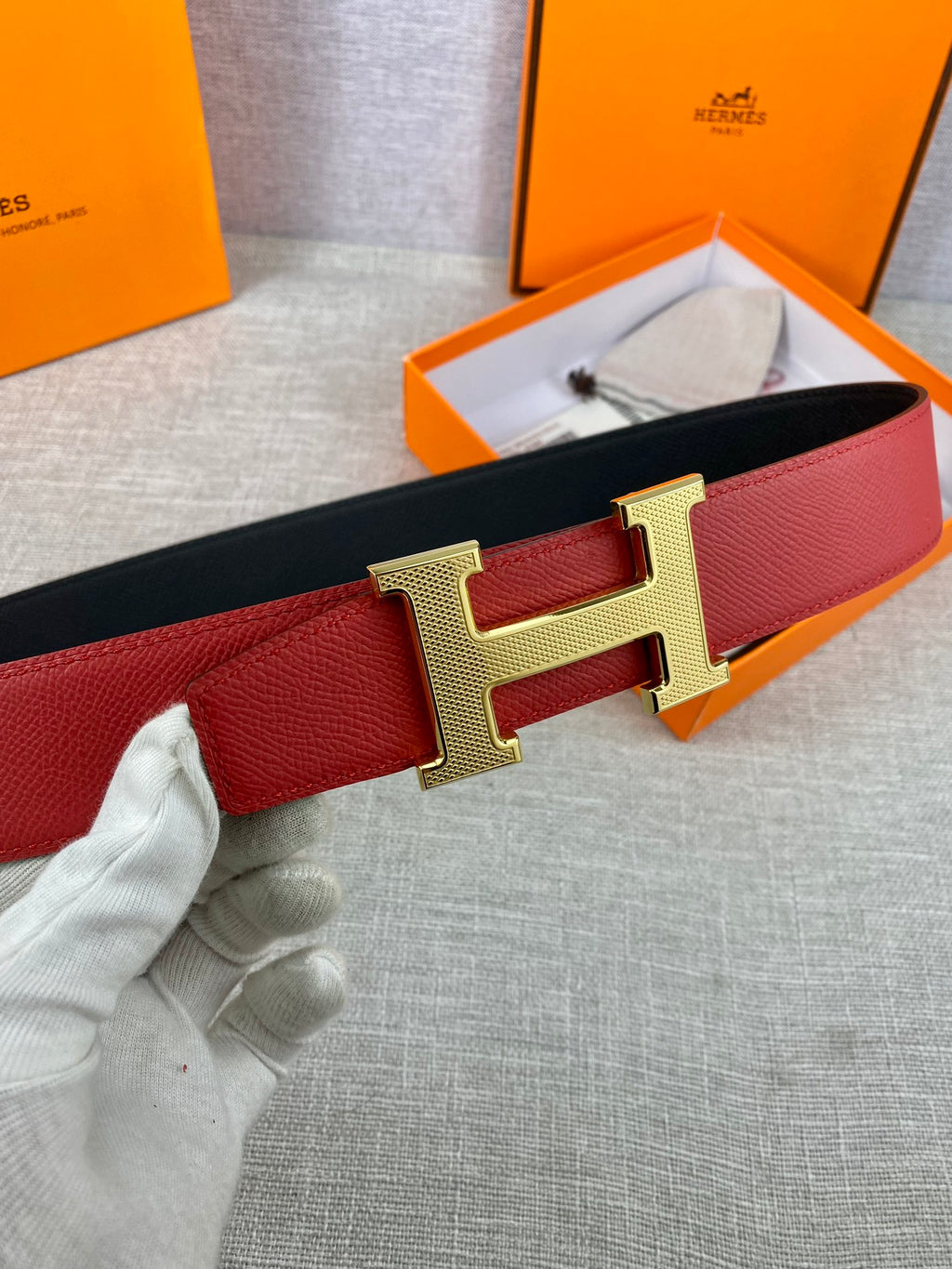 Red leather belt with gold H buckle, close-up