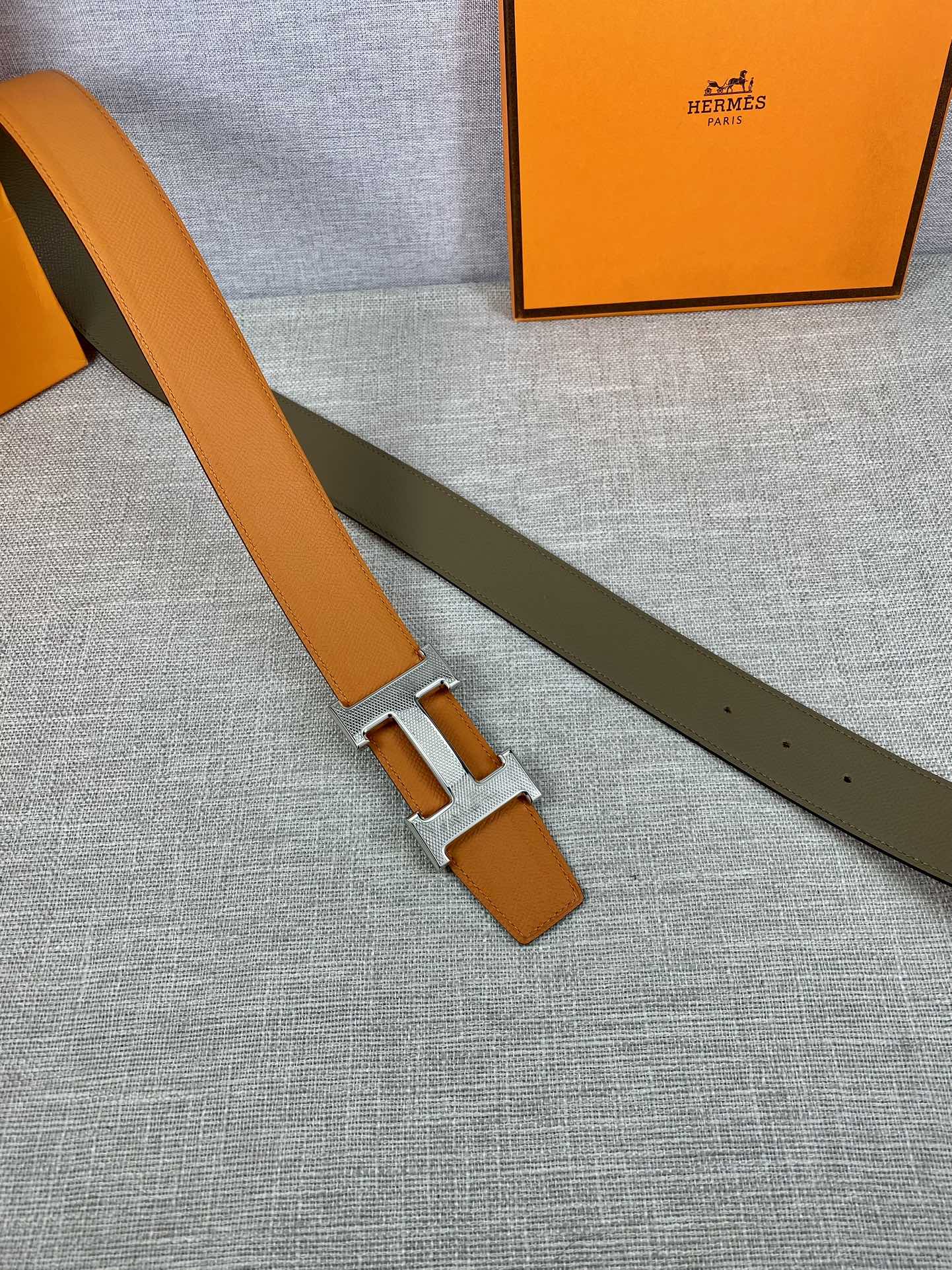 Orange leather belt with silver H buckle and olive keeper strap, laid flat