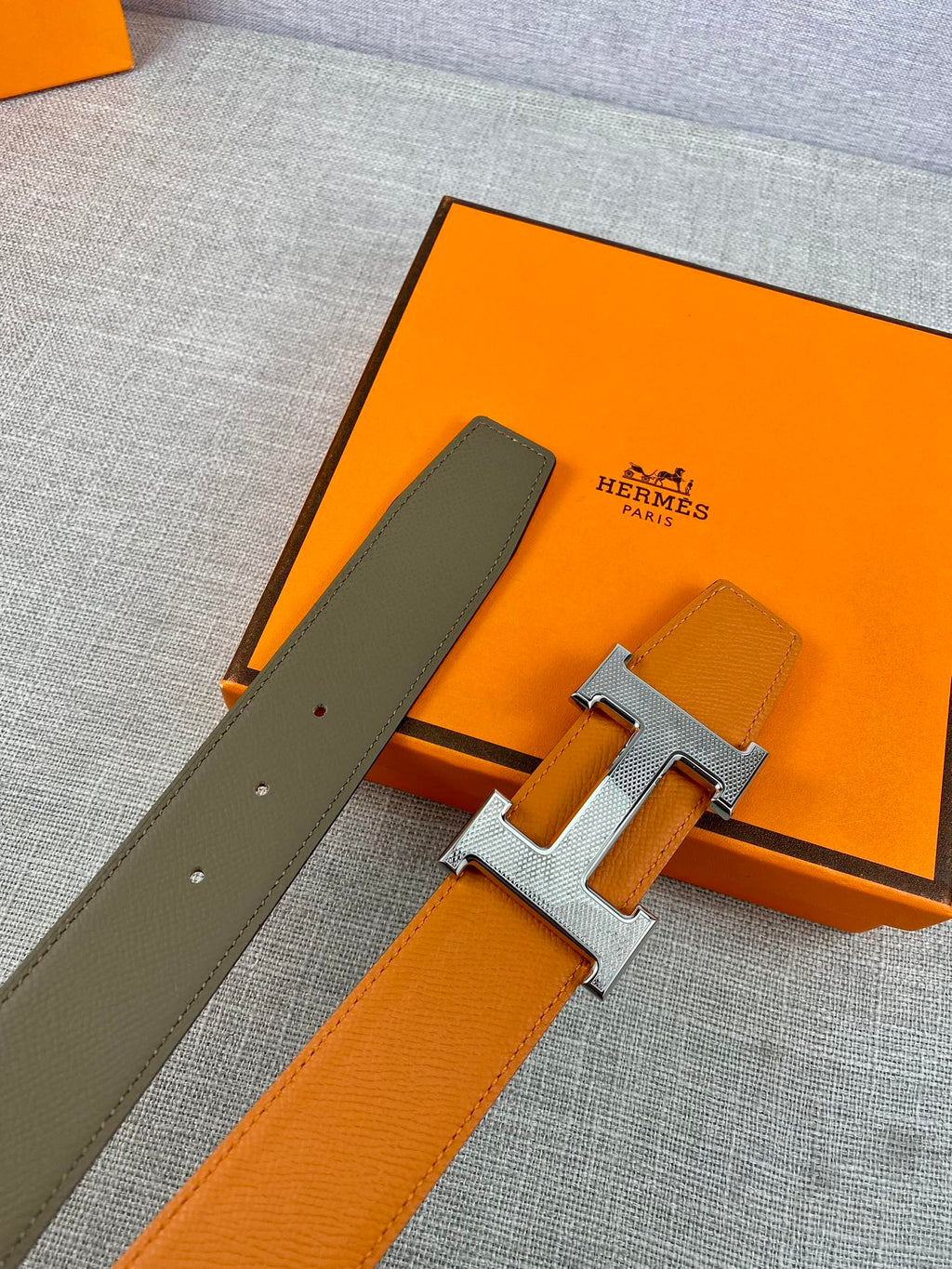 Orange and dark-olive leather belt with gold H buckle, two strap ends visible