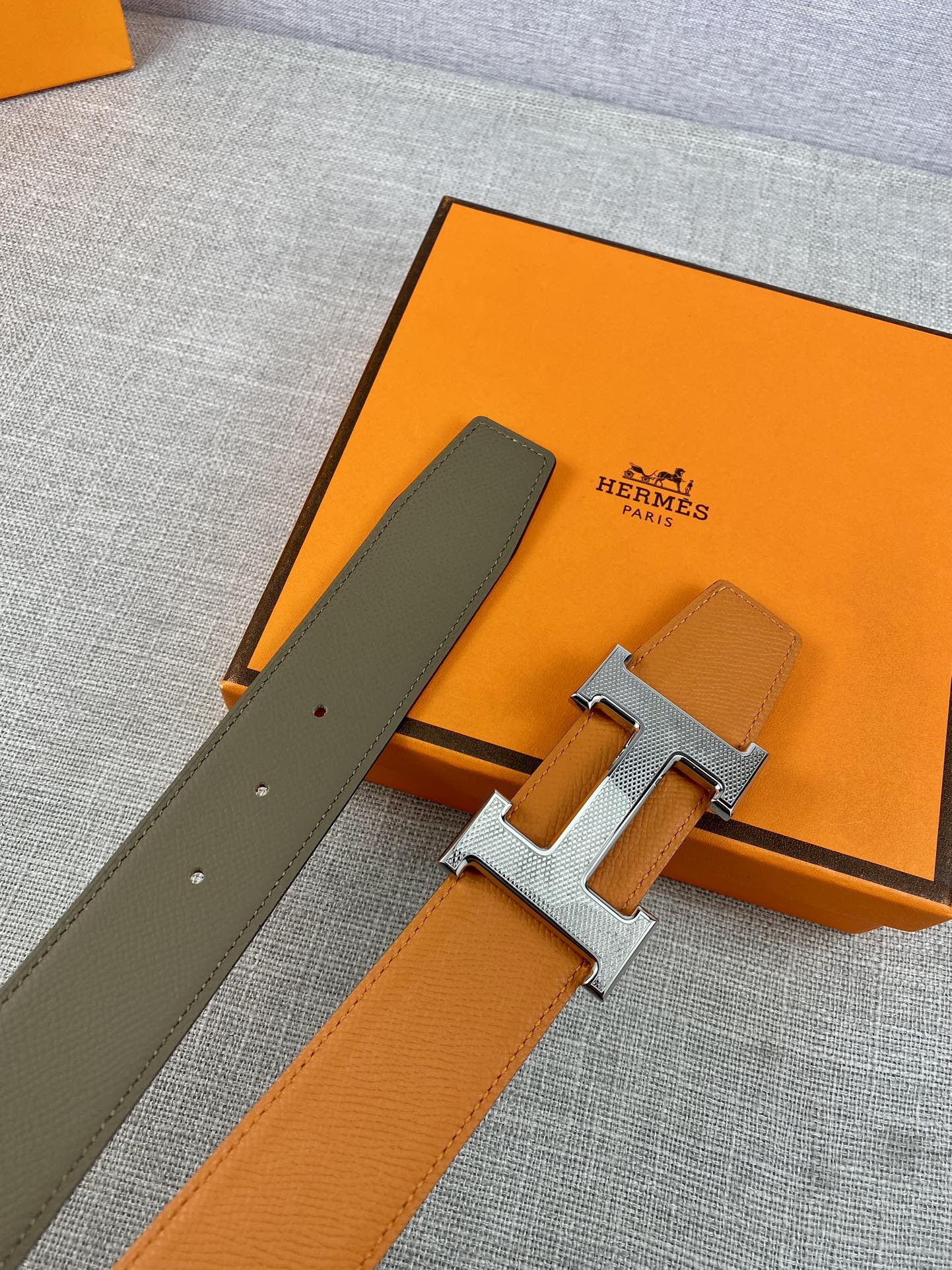 Orange and dark-olive leather belt with gold H buckle, two strap ends visible