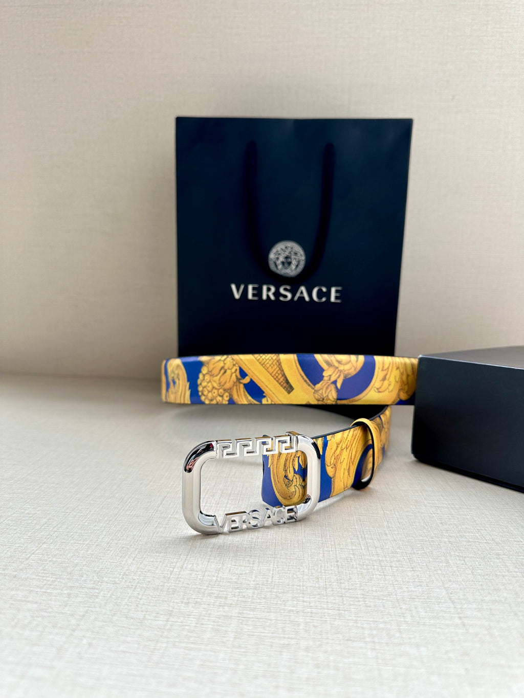 Versace belt with ornate blue-and-yellow print strap and large silver-tone buckle.