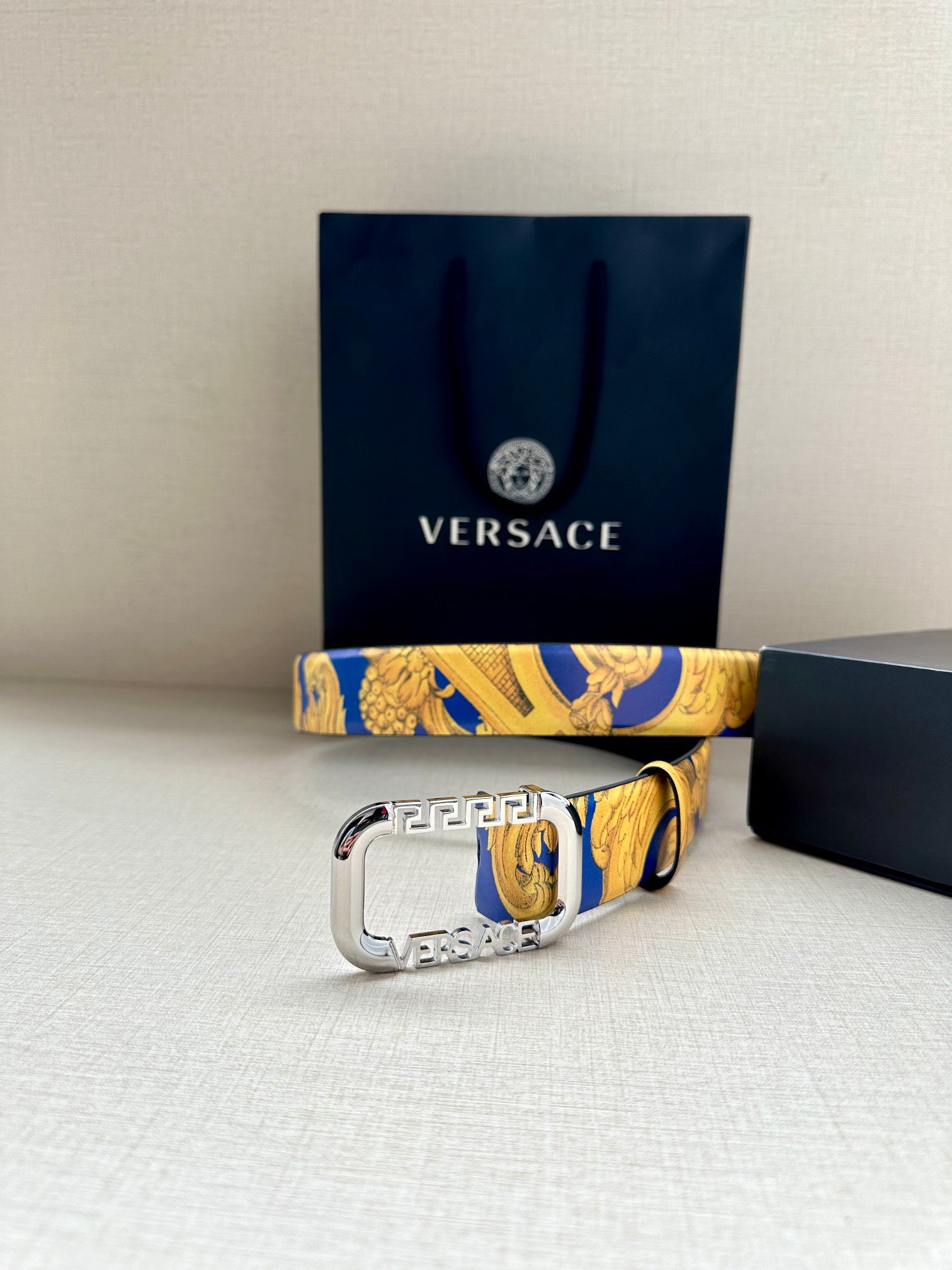 Versace belt with ornate blue-and-yellow print strap and large silver-tone buckle.