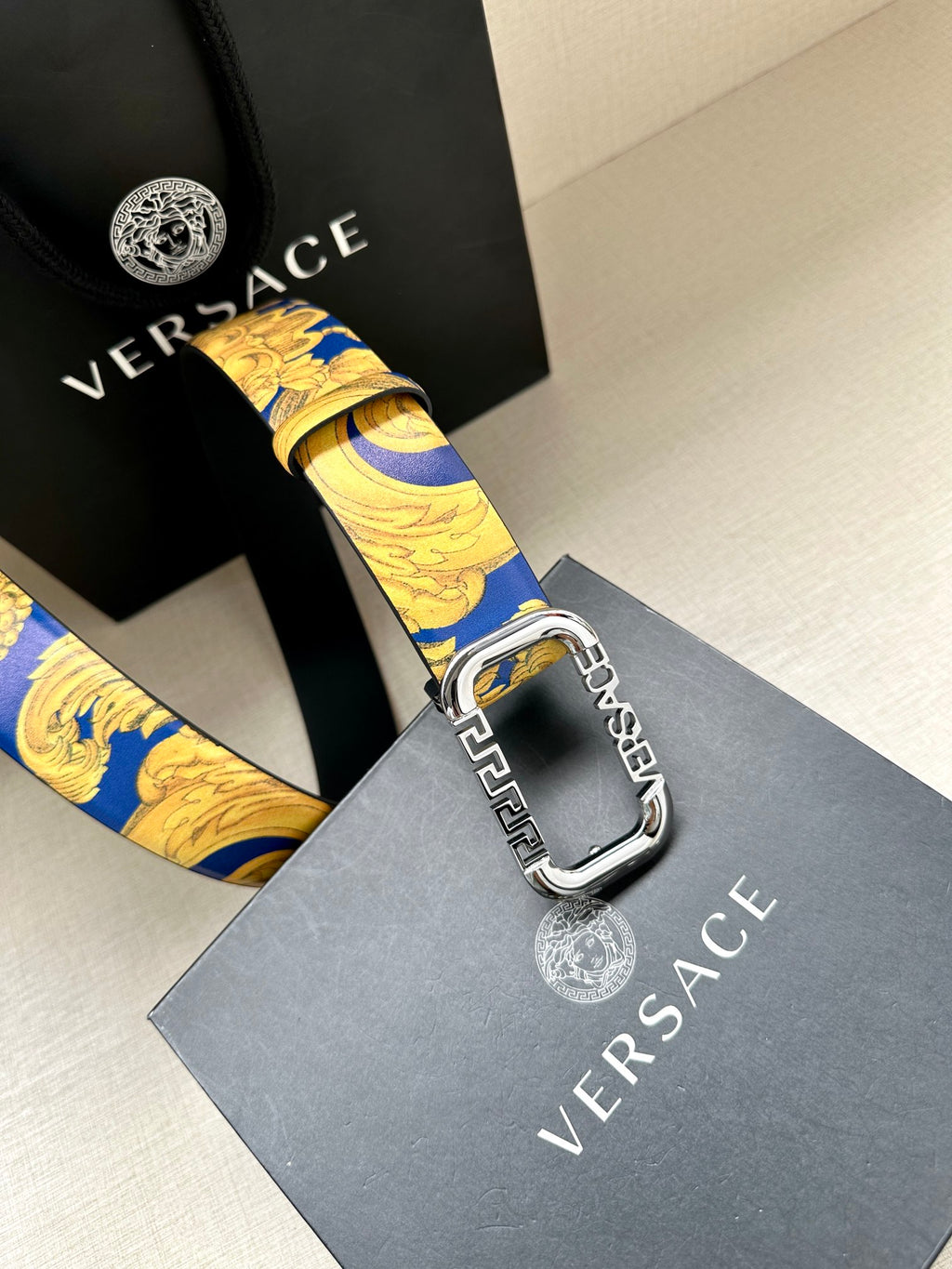 Versace belt detail: blue and gold patterned strap with silver-tone buckle and holes.