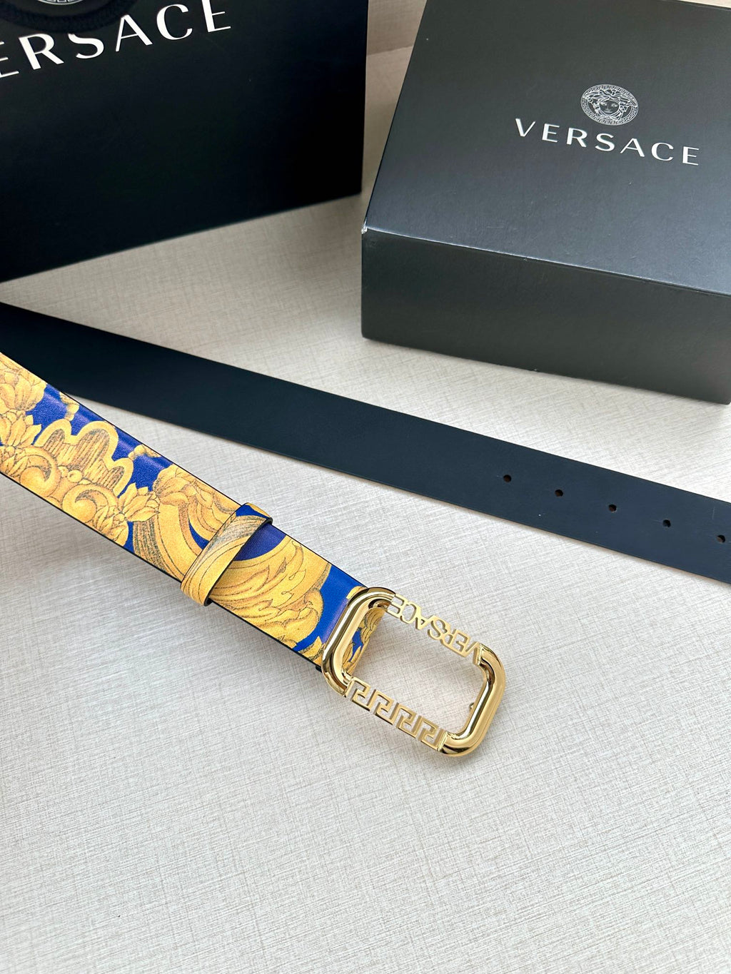 Versace belt laid flat with blue and gold patterned strap and gold-tone square buckle.