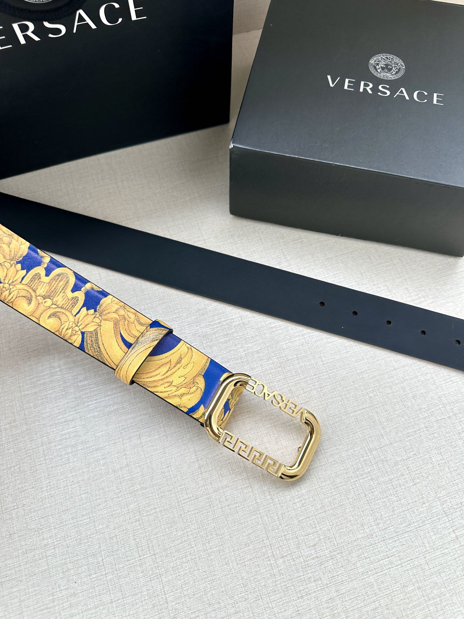 Versace belt laid flat with blue and gold patterned strap and gold-tone square buckle.