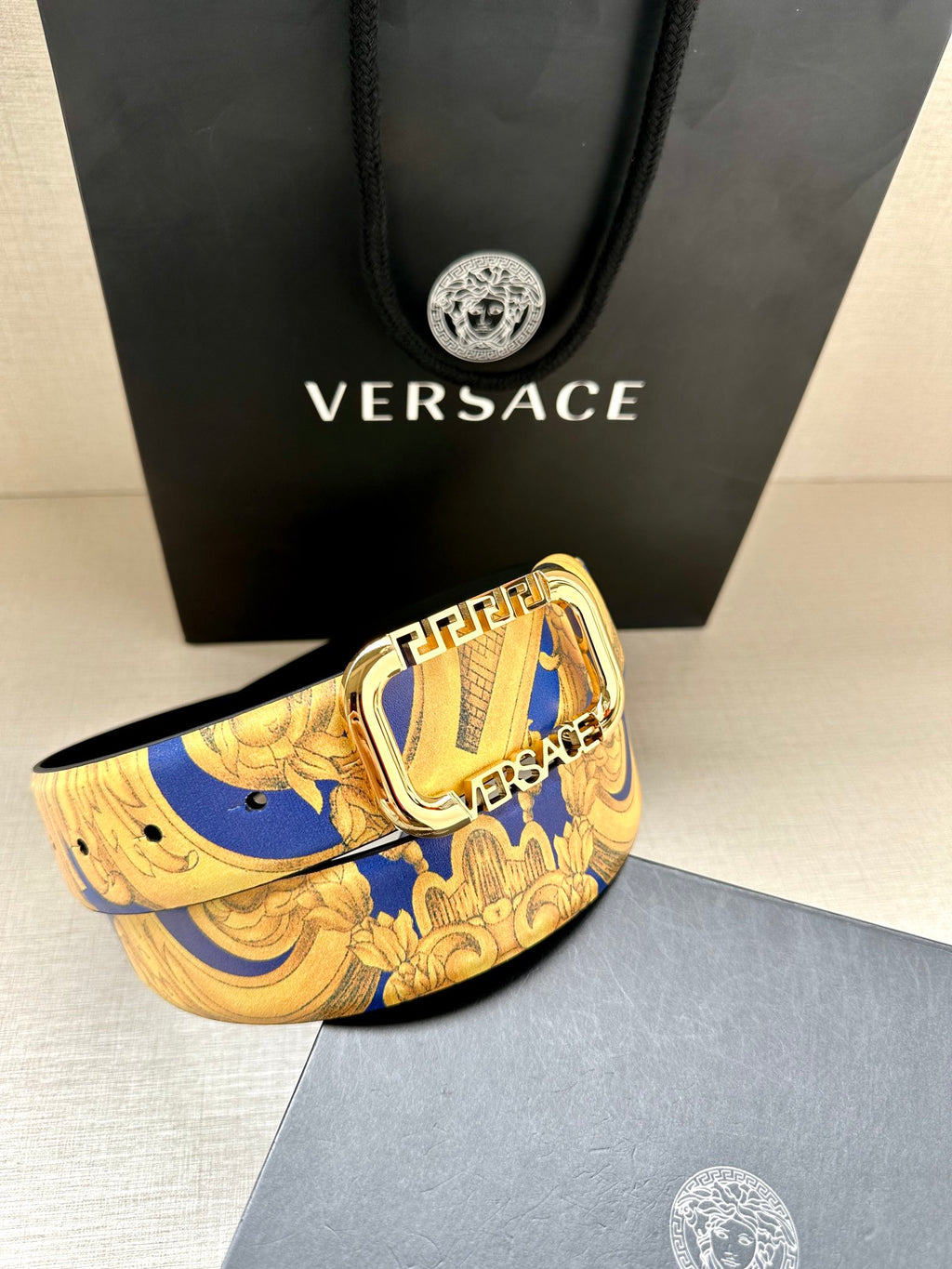 Versace belt close-up with gold-tone buckle on blue and yellow baroque print strap.
