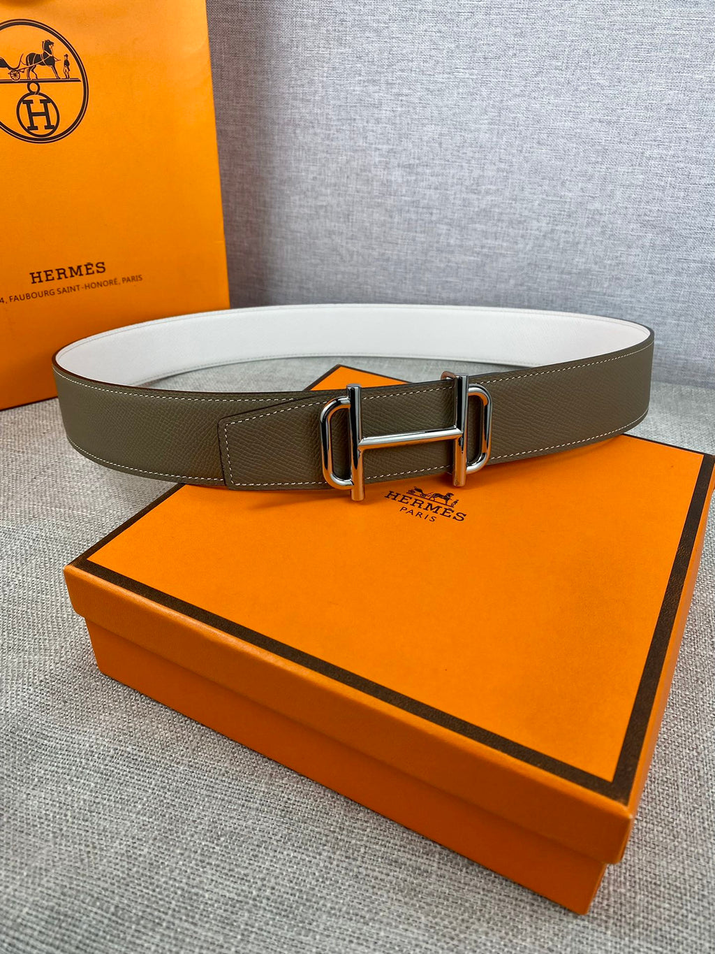 Hermes belt with olive leather strap and gold-tone buckle, laid on display