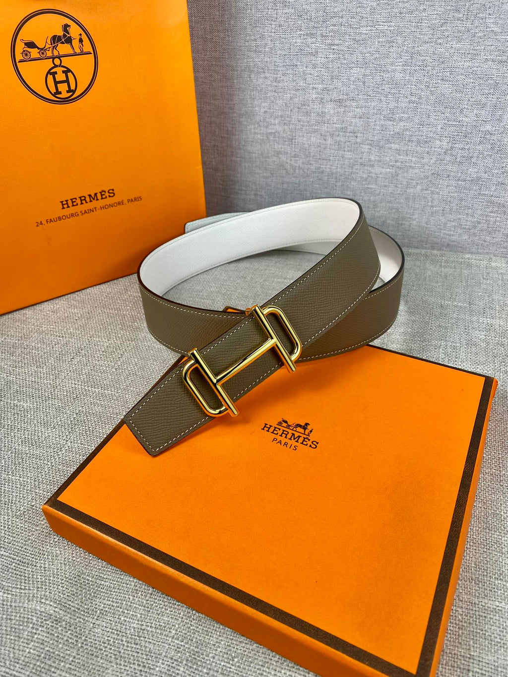 Hermes belt with olive leather and gold-tone buckle, arched on display pad