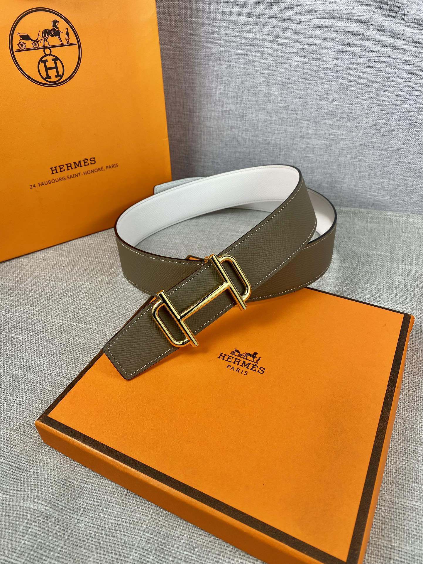 Hermes belt with olive leather and gold-tone buckle, arched on display pad