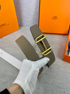 Hermes belt with olive textured leather and gold buckle, laid across white strap