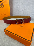 Burgundy leather belt with metallic rectangular buckle lying on a surface