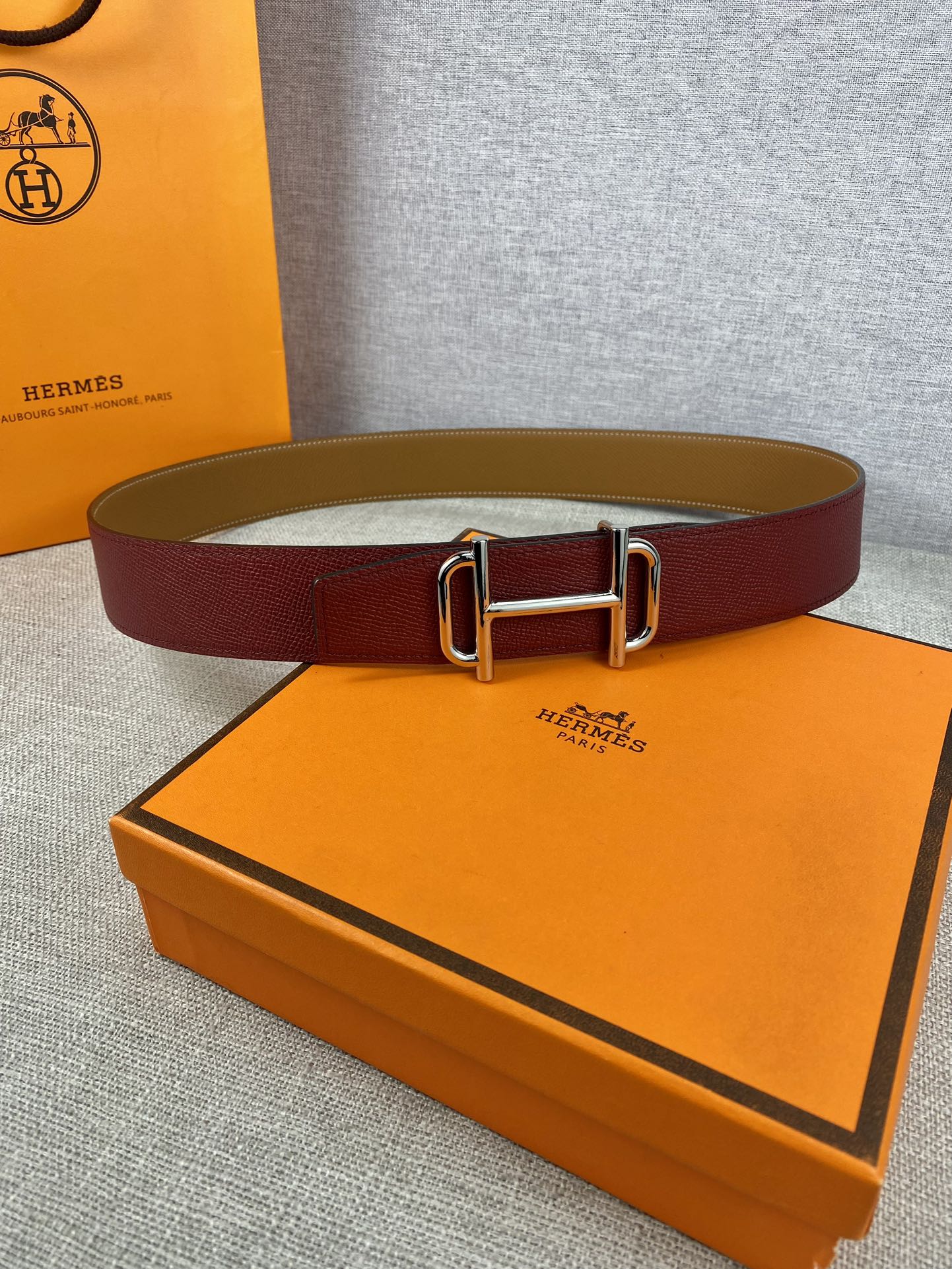 Burgundy leather belt with metallic rectangular buckle lying on a surface