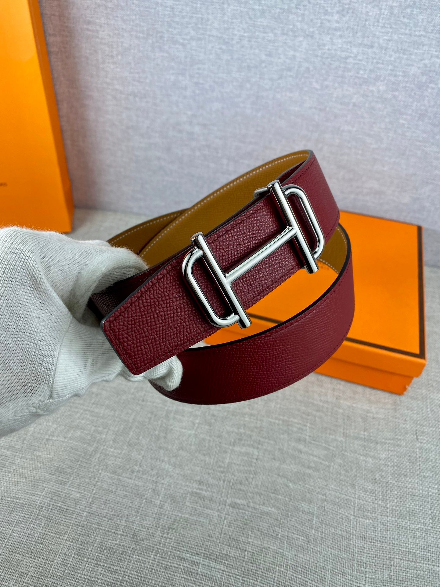Burgundy leather belt with metallic double-prong buckle and textured strap