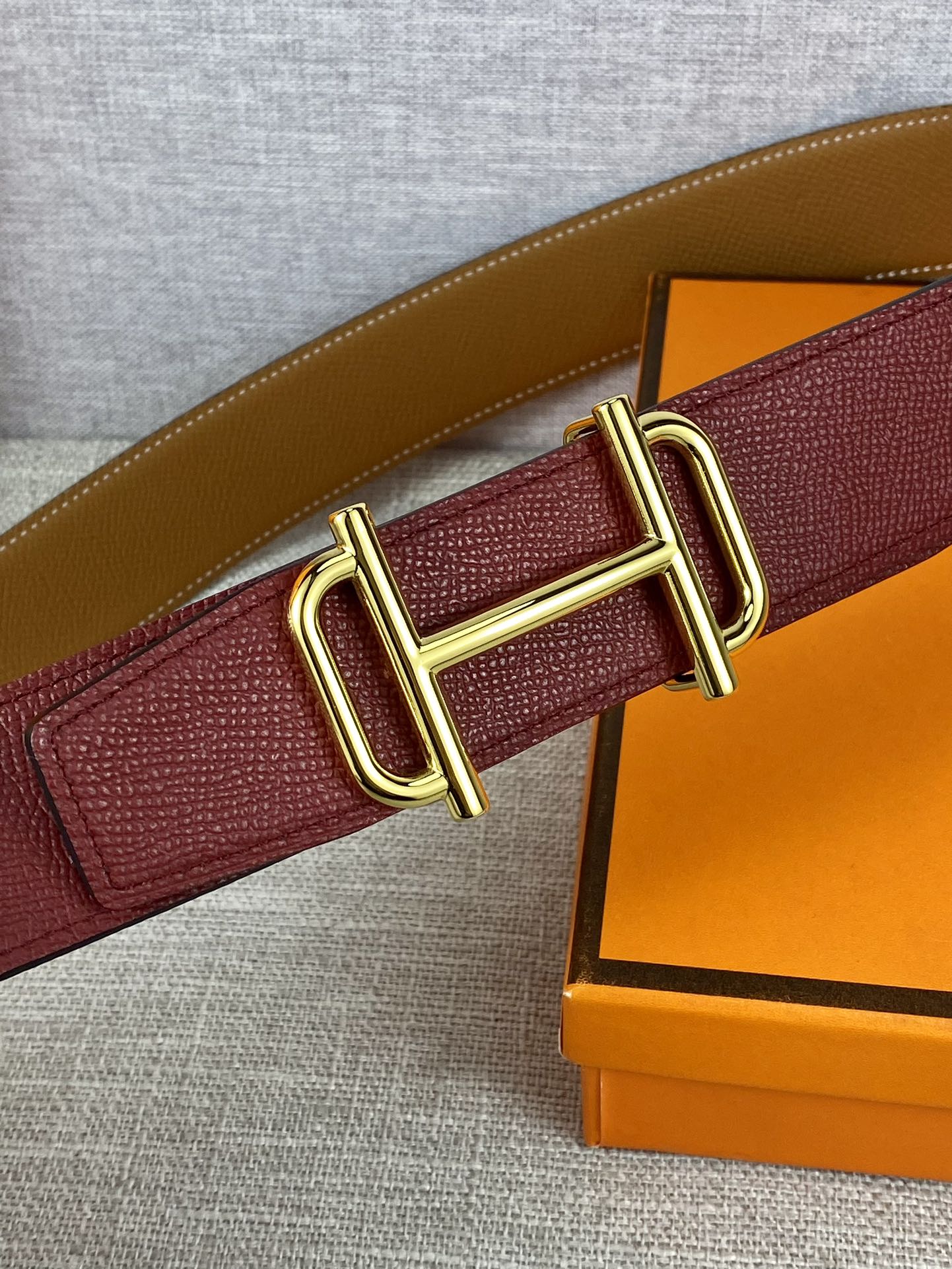 Burgundy leather belt close-up with gold-tone rectangular buckle and textured strap