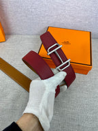 Burgundy leather belt held in hand, showing metallic double buckle